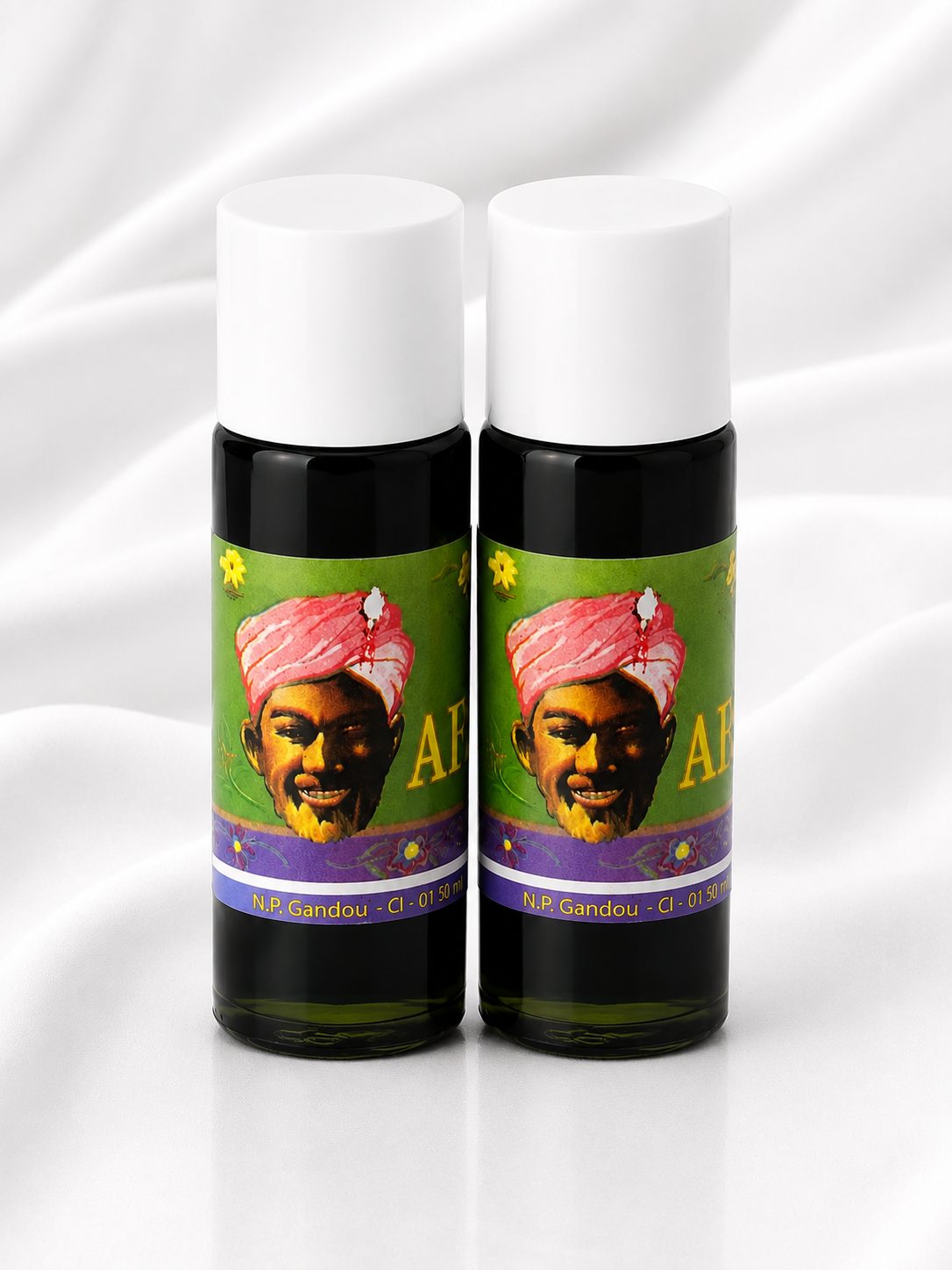 Two small cylindrical bottles with white caps and dark bodies, standing side by side on a white draped fabric background. Each bottle has a colorful label featuring a portrait of a man in a pink turban and the text 'AI BANDOU'.