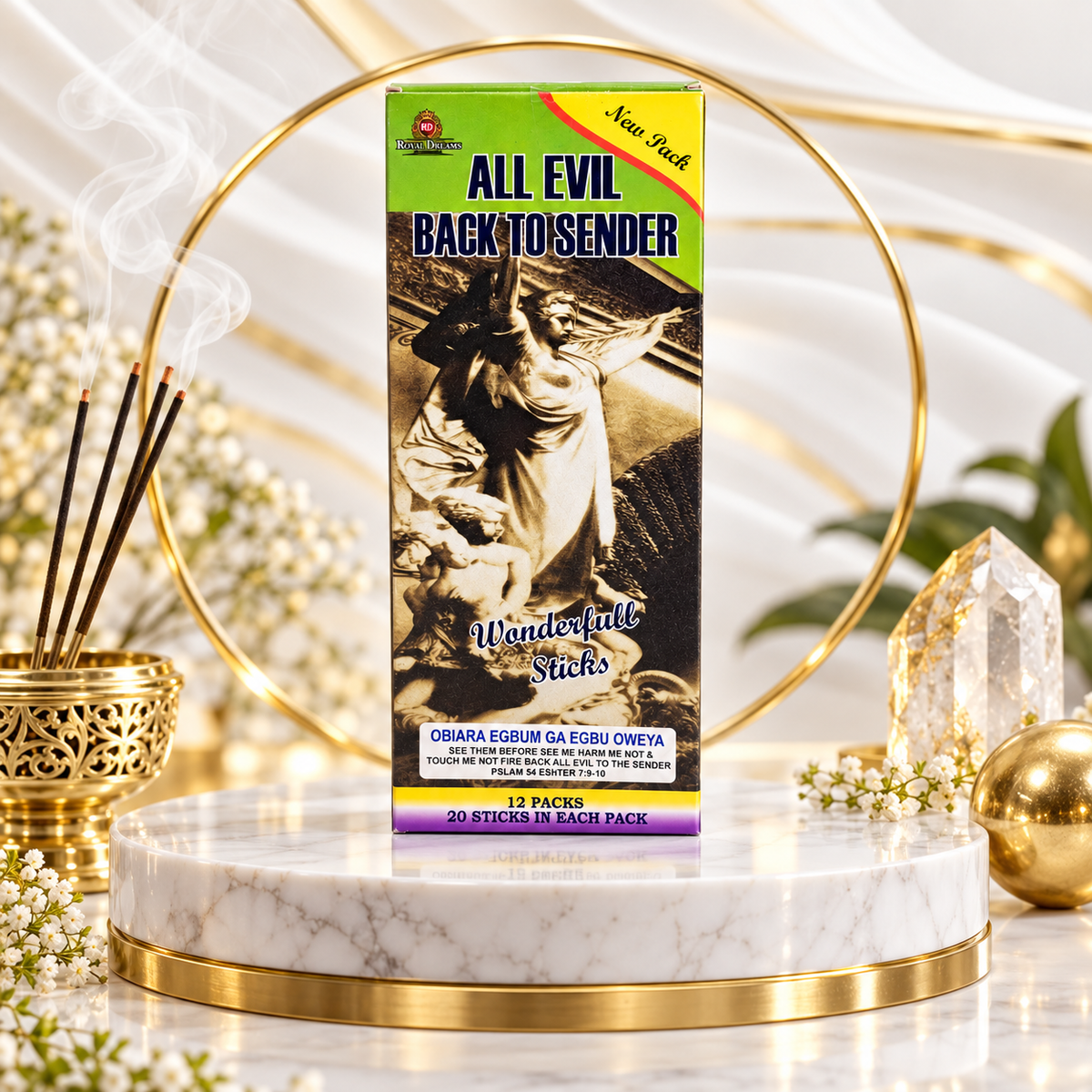 A boxed incense stick product labeled 'ALL EVIL BACK TO SENDER' stands on a white marble pedestal with gold trim, surrounded by decorative props including a gold incense holder with smoking sticks, white flowers, crystals, and a gold sphere. The box has a green top, black central artwork, and purple text near the bottom.