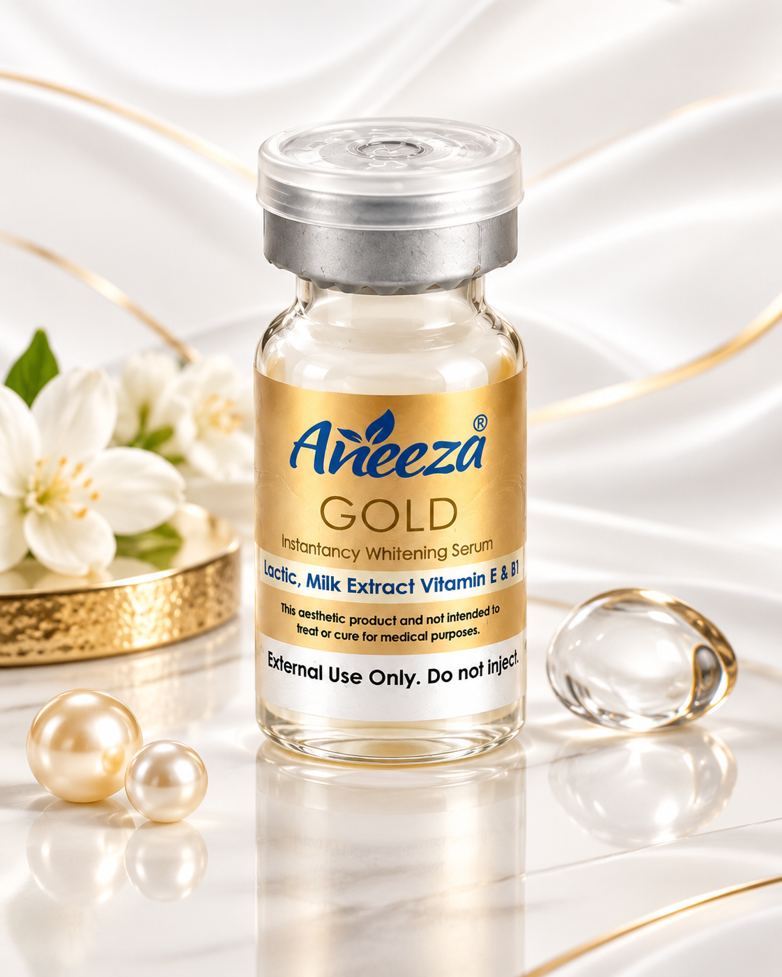 A vial of Aneeza Gold Instantancy Whitening Serum, a clear glass bottle with a gold label and silver cap, styled on a white reflective surface with decorative pearls, flowers, and a gold capsule.