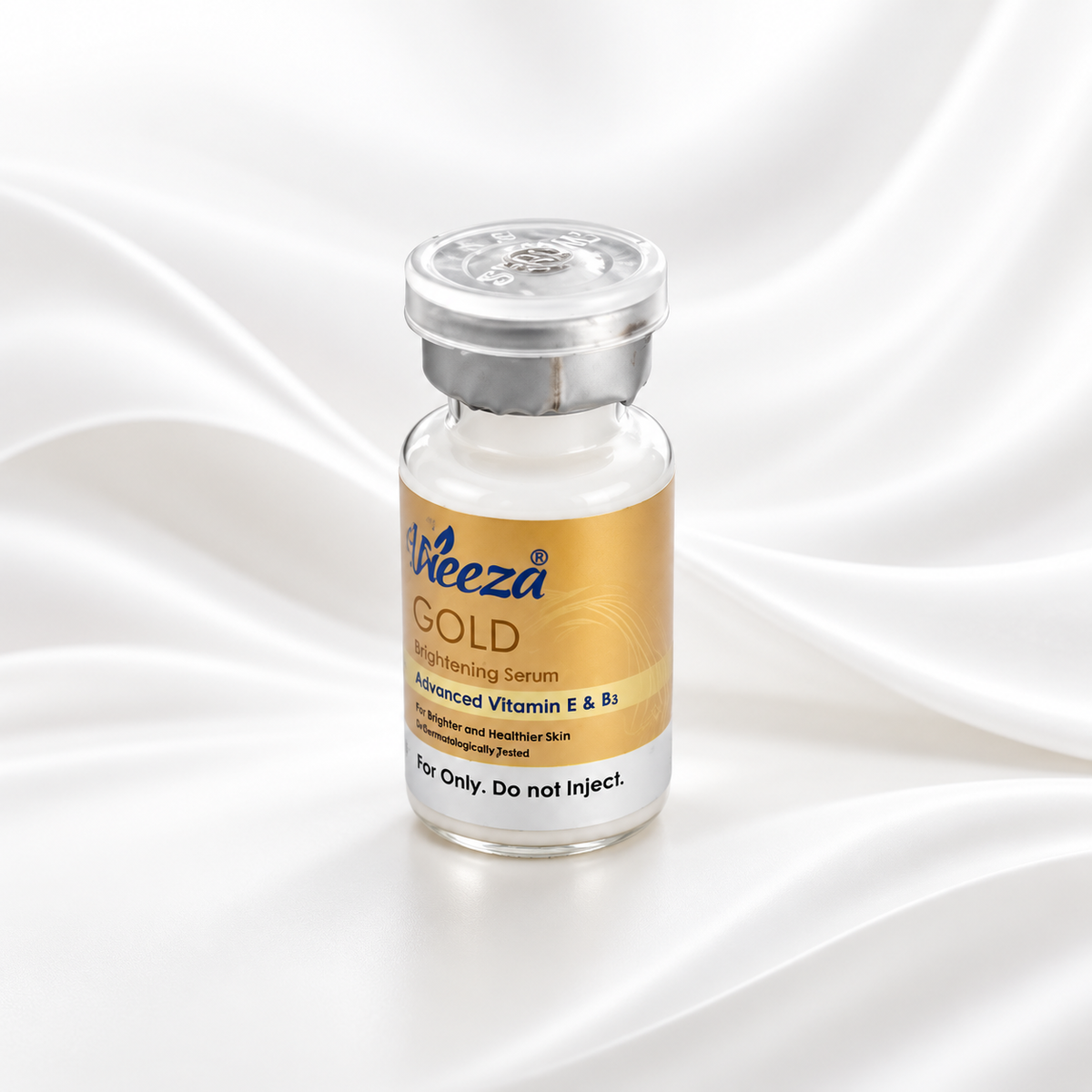 A small glass vial of Weeza Gold Brightening Serum with a metallic gold label and silver cap, set against a draped white satin background.