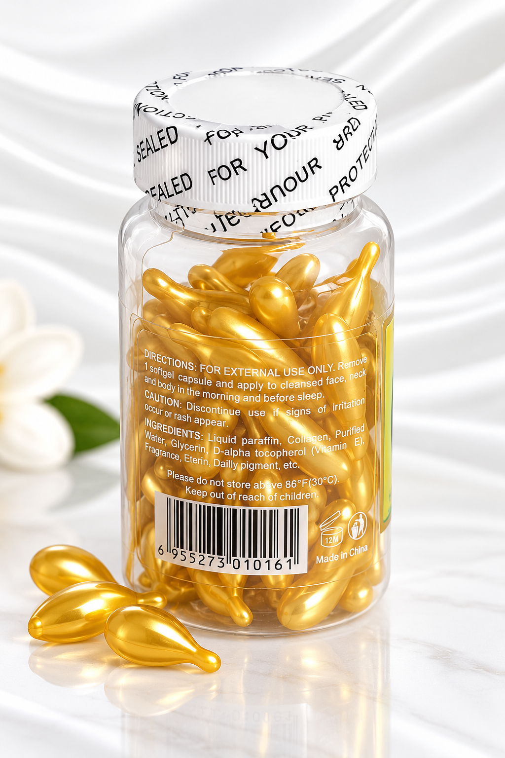 A clear plastic bottle filled with shiny gold teardrop-shaped capsules, sealed with a white branded cap, on a white marble-like surface with a few capsules placed in front.
