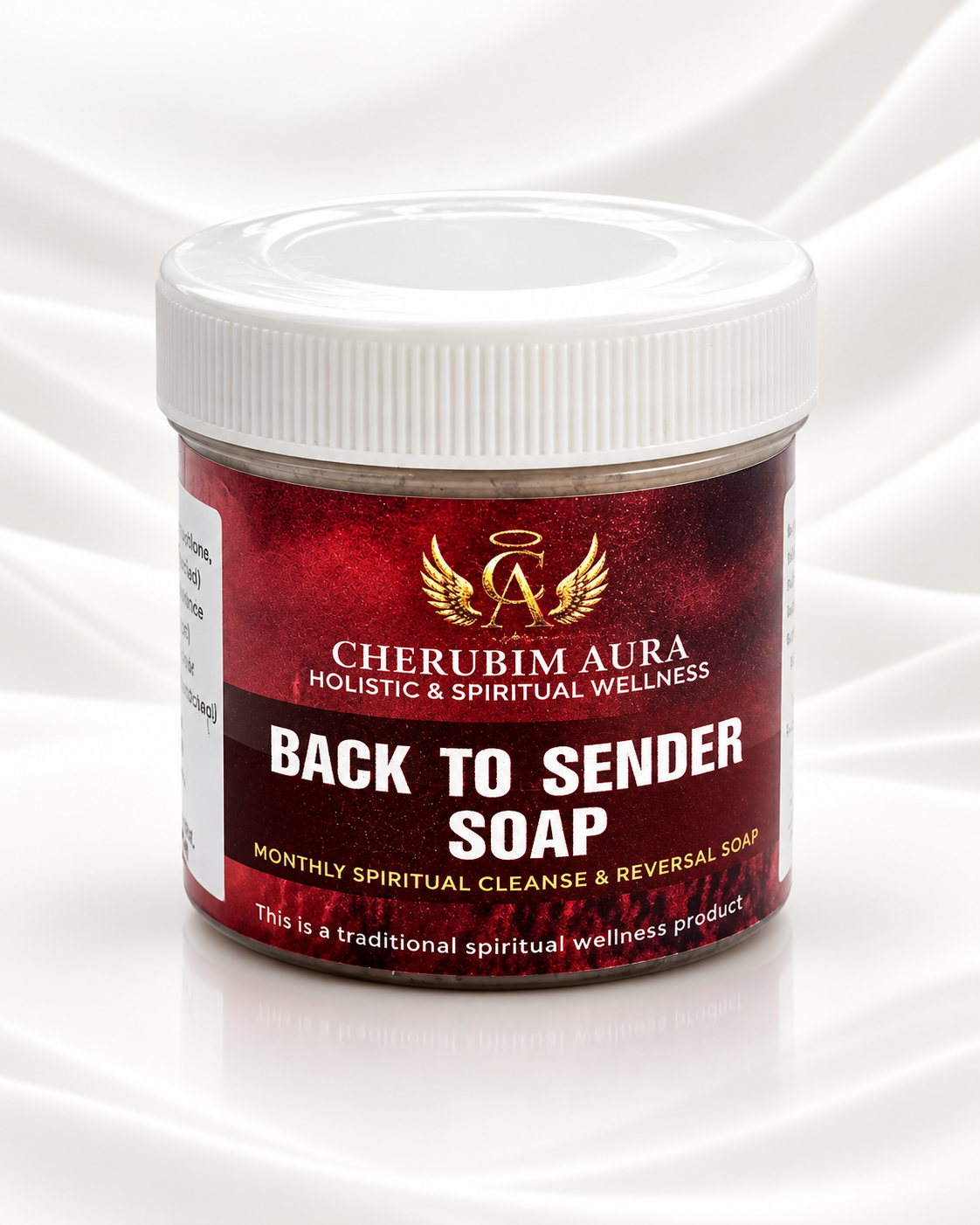 A jar of Cherubim Aura Back to Sender Soap on a white satin background. The product is in a clear plastic jar with a white screw-on lid and a red label featuring gold and white text.
