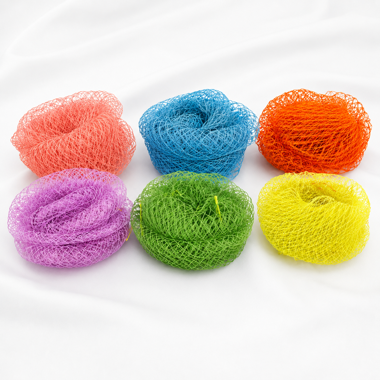 Six mesh bath sponge balls in assorted colors including orange, blue, red, purple, green, and yellow, arranged in two rows on a white fabric background.