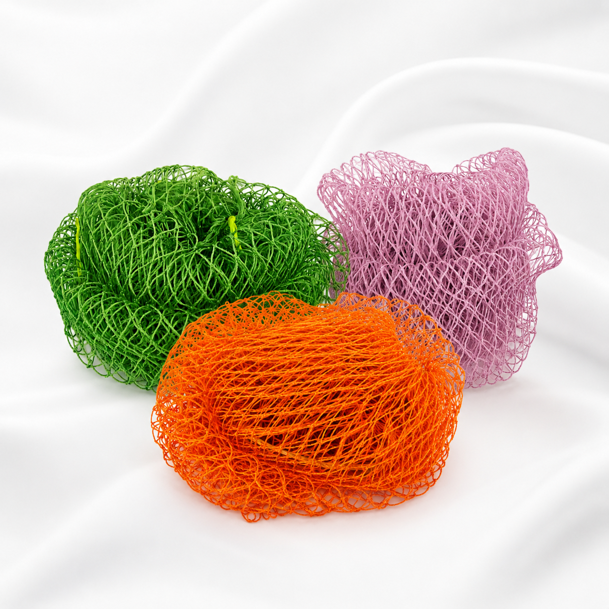 Three mesh netting balls in green, orange, and pink, arranged on a white draped fabric background.