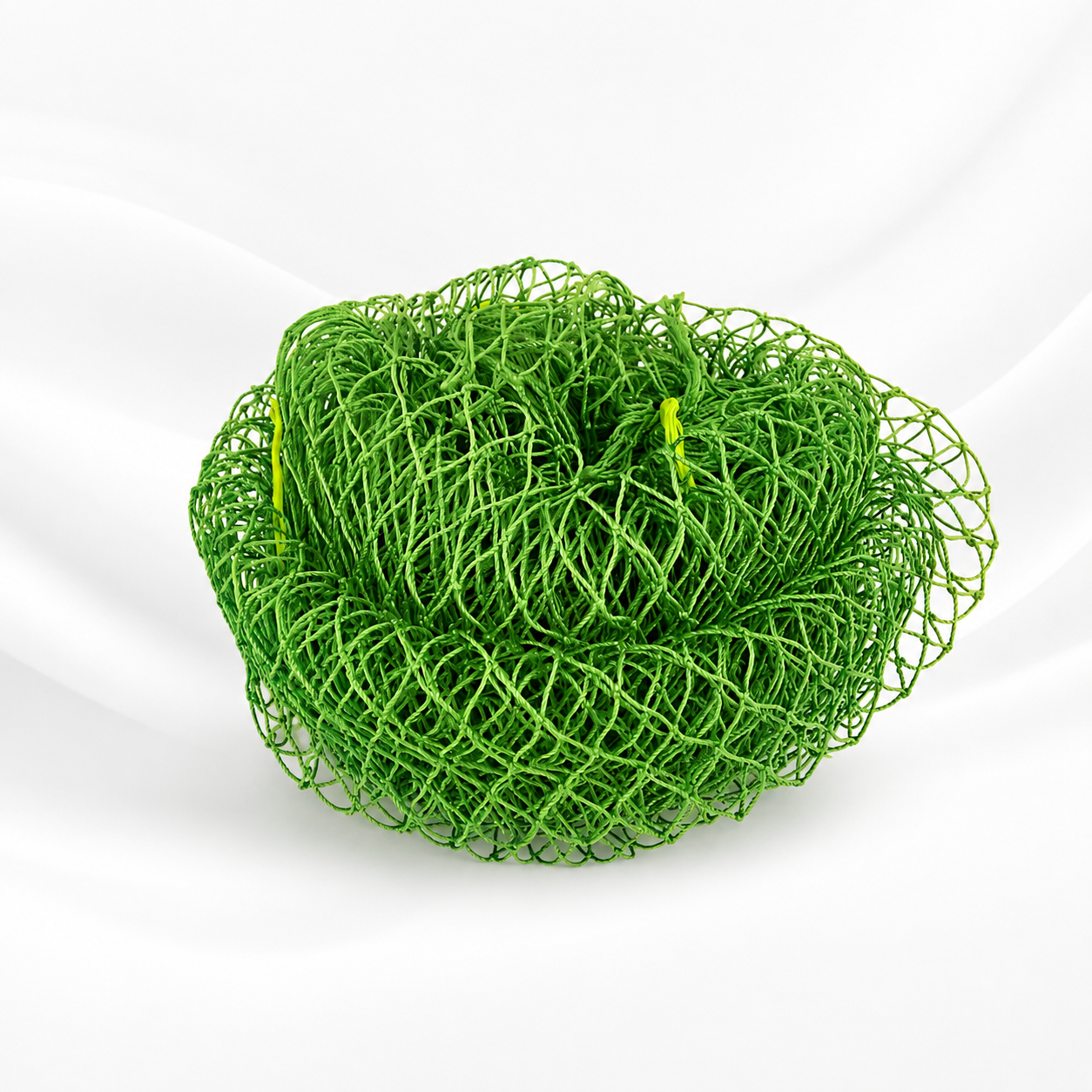 A coiled bundle of bright green mesh netting material, photographed against a clean white studio background with soft draped fabric behind it.
