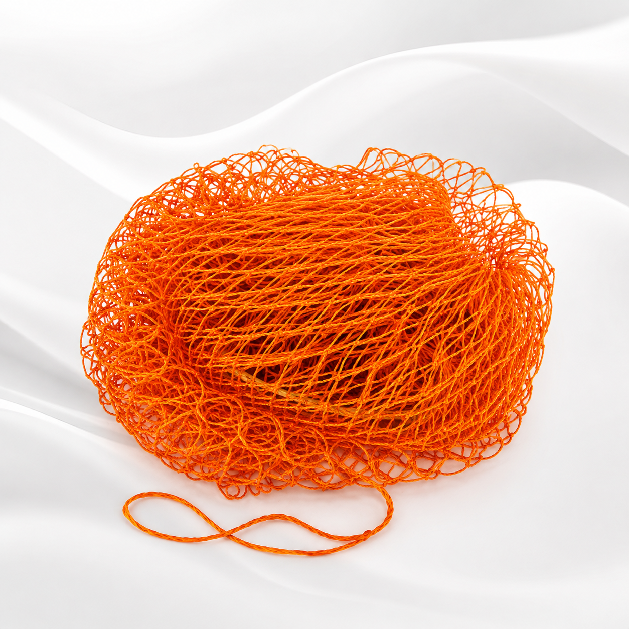 Bright orange ball of twisted thread or cord, photographed on a clean white draped fabric background.
