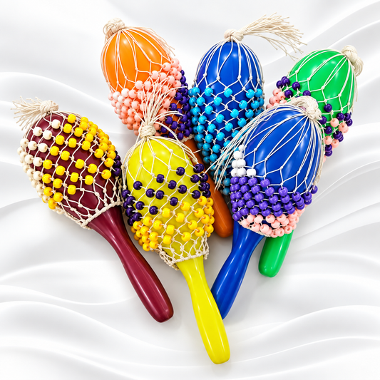 Six colorful maracas arranged on a white satin-like fabric background. The maracas have smooth handles in red, yellow, blue, green, orange, and purple, decorated with white netting and rows of beads in matching colors.