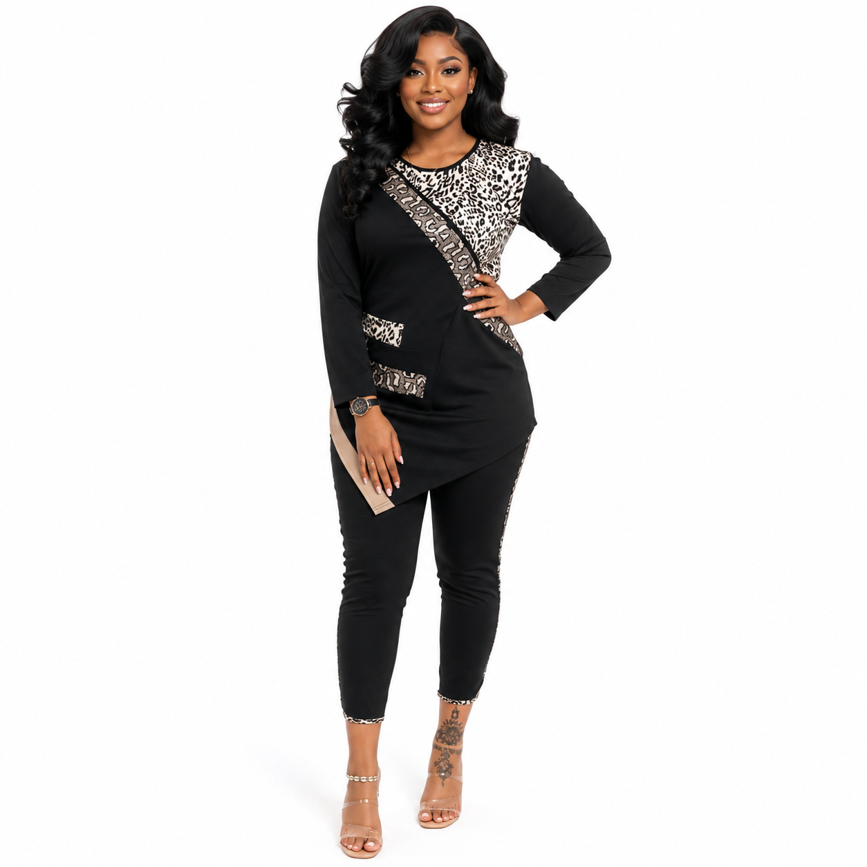 A woman modeling a black long-sleeve jumpsuit with leopard print panels on the chest and hip, paired with black skinny pants and nude high-heeled sandals, against a plain white background.