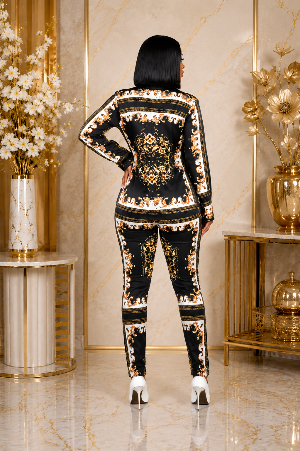 A woman stands with her back to the camera wearing a black long-sleeve jumpsuit with an ornate gold and beige baroque-style pattern. She is posed in a luxurious room with gold accents, marble floors, and decorative vases.
