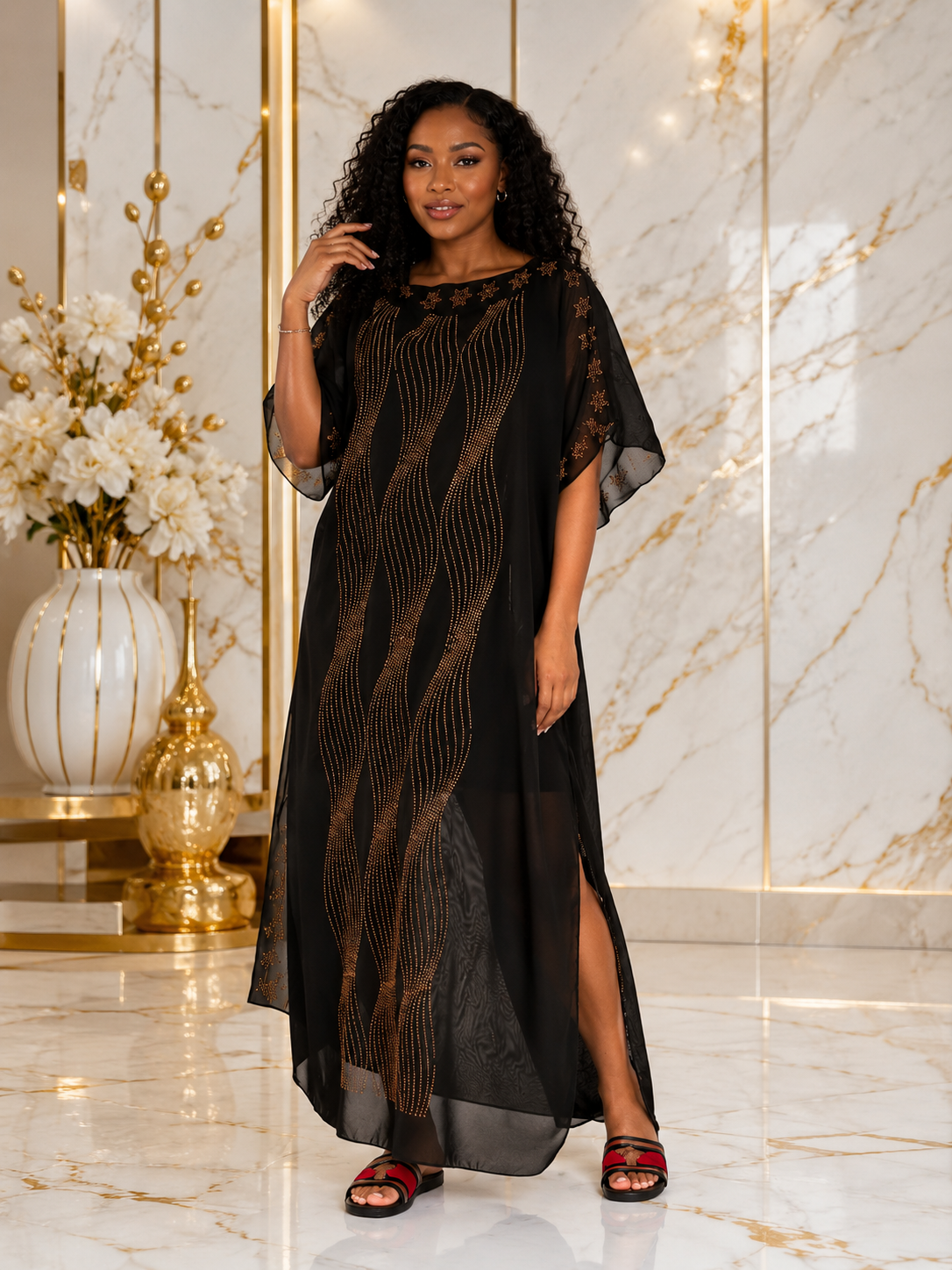 A woman modeling a black sheer maxi dress with gold vertical wavy stripes, standing in a luxurious room with marble floors and gold accents.