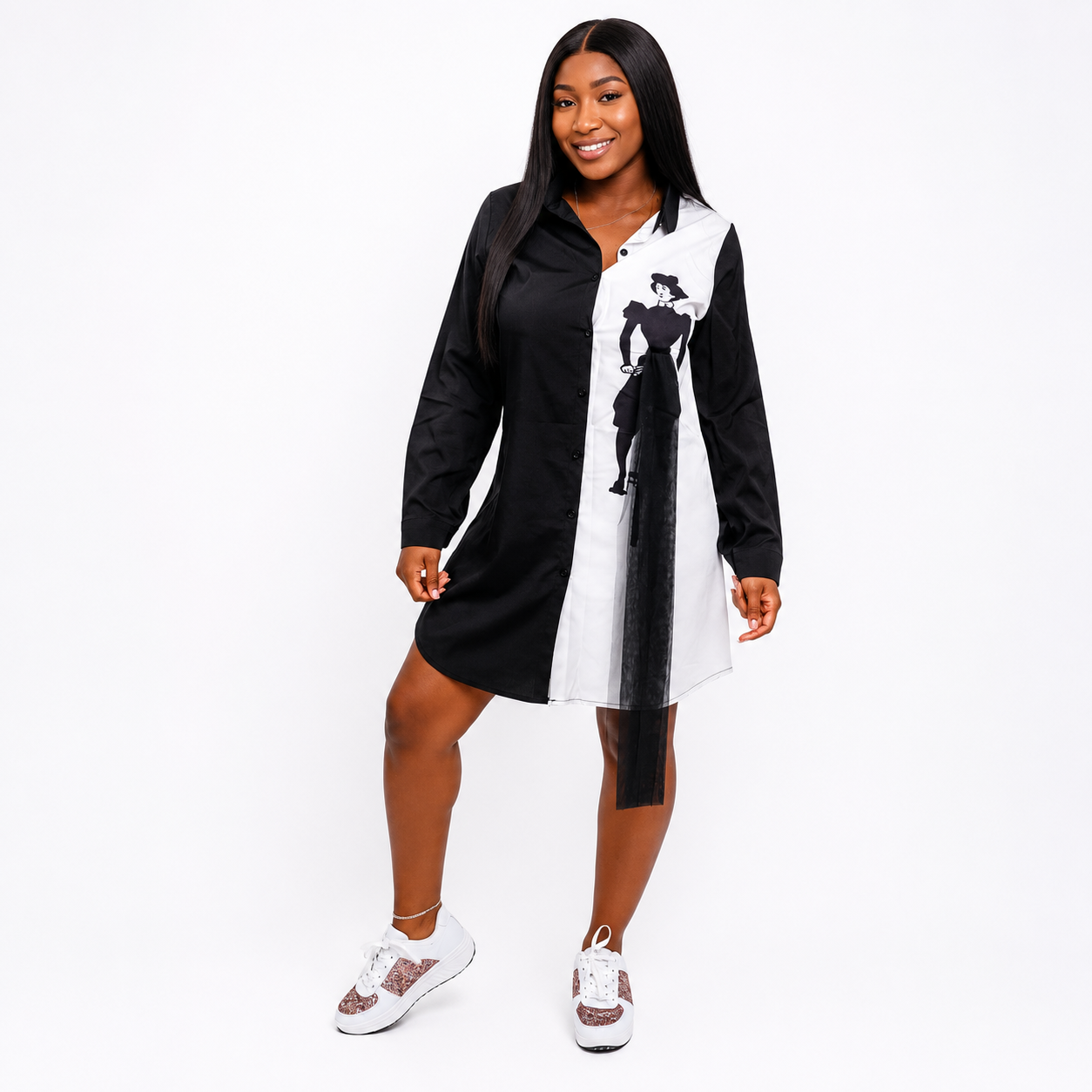 A woman modeling a long-sleeve mini dress with a black and white color-blocked design and a black graphic print on the white side, paired with white sneakers, against a plain white background.