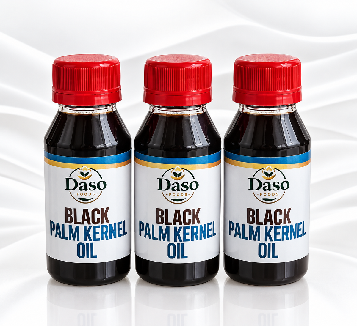 Three bottles of Daso Palm Kernel Oil arranged side by side on a white background with a soft draped fabric texture behind them. The bottles are filled with very dark oil, have red caps, and white labels with blue and gold accents.