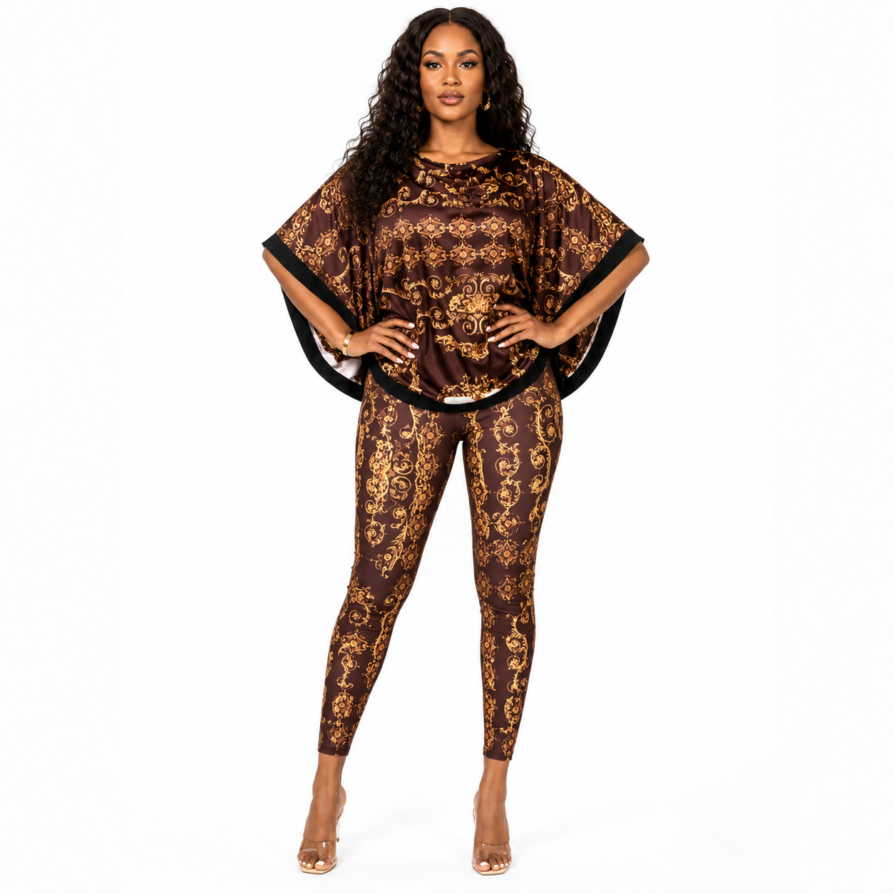 A woman modeling a matching two-piece outfit featuring a brown and gold baroque patterned top with wide draped sleeves and matching patterned leggings, set against a plain white background.
