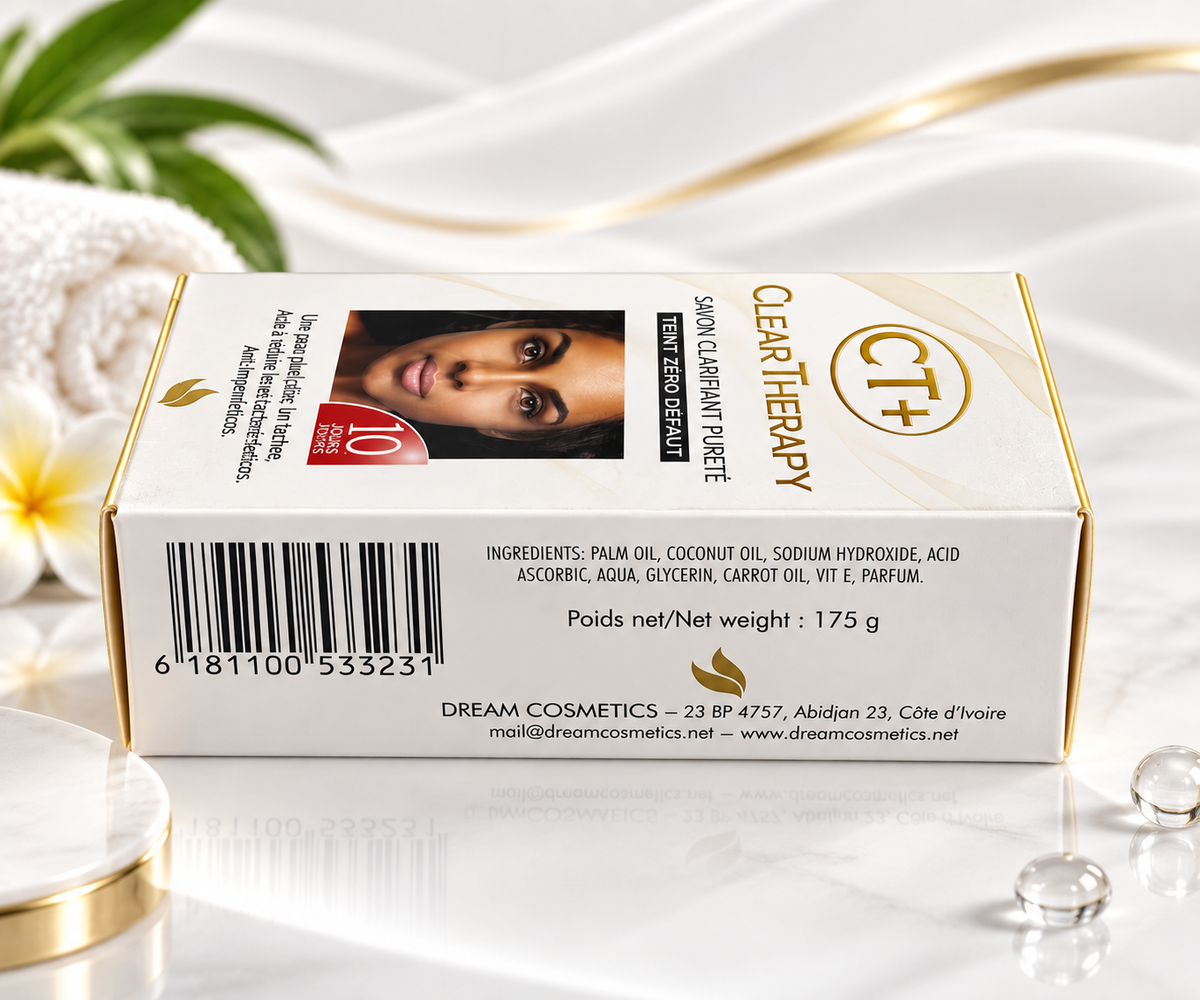 A box of Dream Cosmetics Clear Therapy CT+ hair oil, featuring a white and gold design with a photo of a woman's face on the front, set on a reflective white surface with decorative gold and white elements.