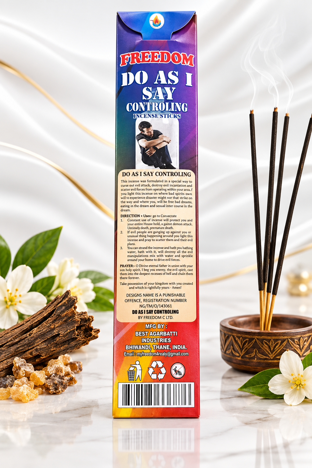 A boxed incense stick product standing upright on a white marble surface, with incense sticks in a small bowl and flowers around it. The box is labeled 'FREEDOM DO AS I SAY CONTROLLING' and shows a colorful gradient design with text and a barcode.