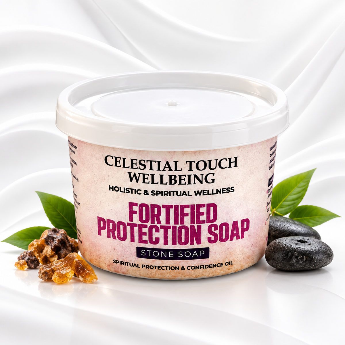 A tub of Celestial Touch Wellbeing Fortified Protection Soap on a white draped background, styled with amber resin pieces, dark stones, and green leaves.