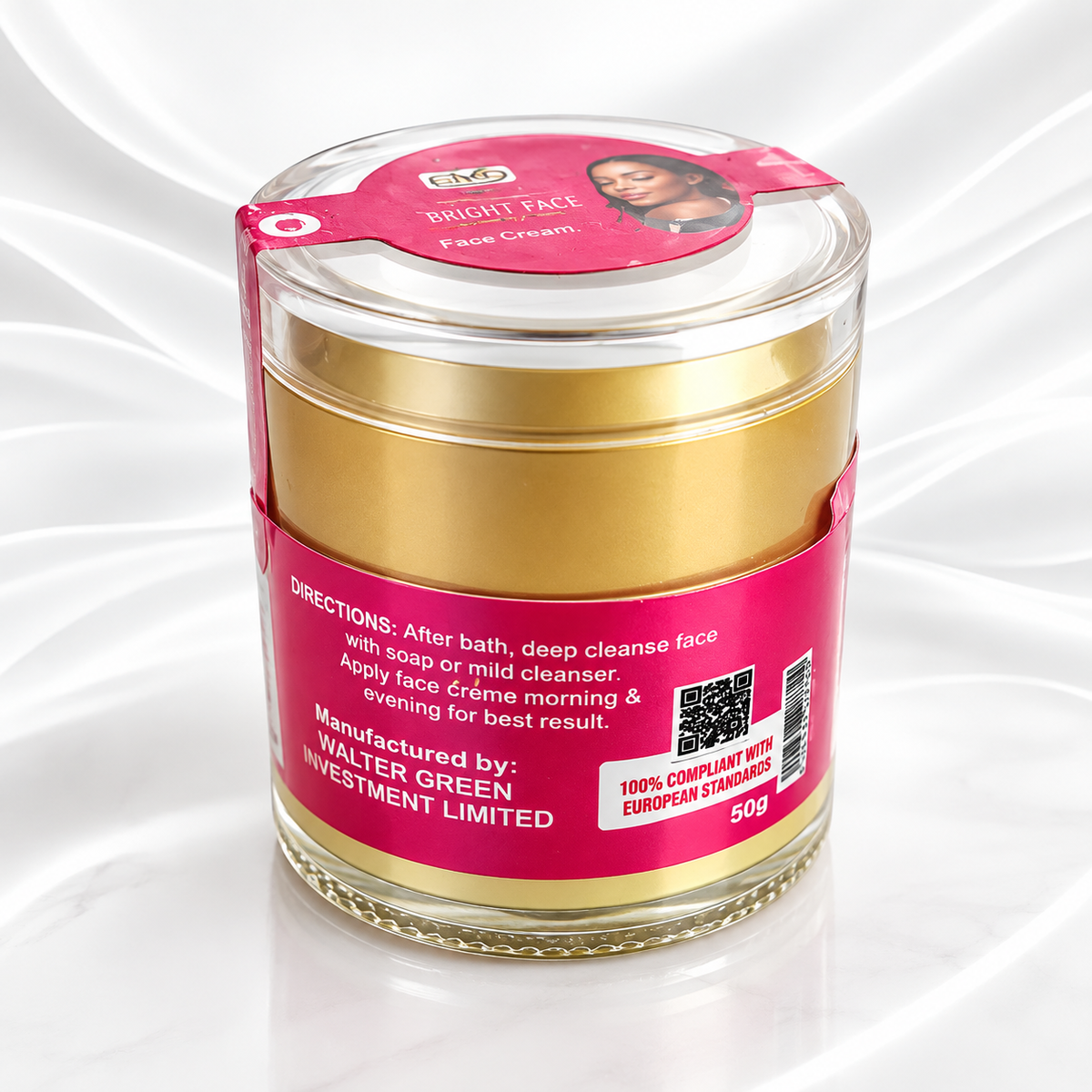 A jar of Walter Green Investment Limited Bright Face Face Cream, featuring a gold-colored cream inside a clear glass jar with a bright pink label and a matching pink lid seal, set against a white satin background.