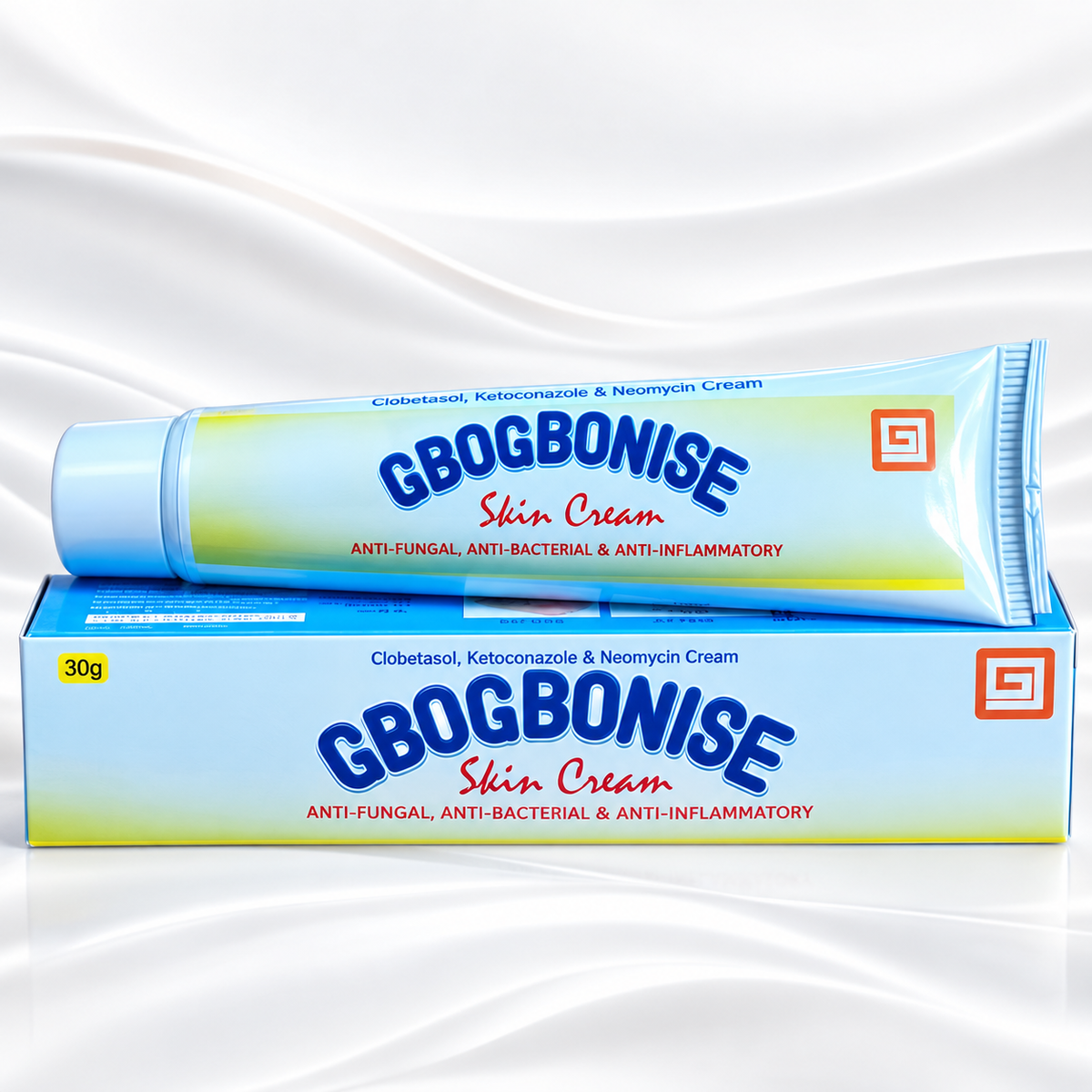 A tube of GBOGBONISE Skin Cream resting on top of its matching blue and white box, set against a white satin fabric background.
