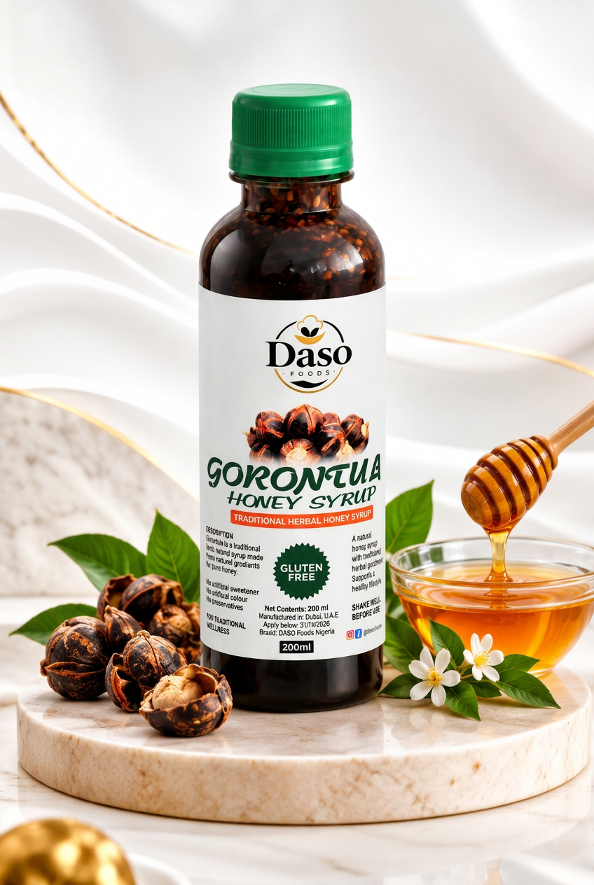 A bottle of Daso Gorontua Honey Syrup stands on a marble slab with a honey dipper, honey bowl, and jatropha pods around it against a white draped backdrop.