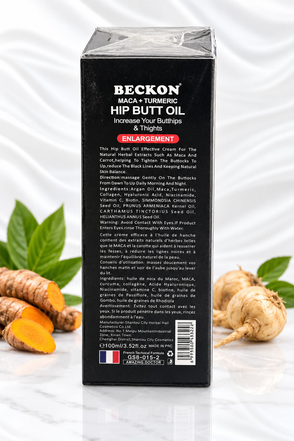 A black rectangular box of Beckon Maca + Turmeric Hip Butt Oil stands upright on a white reflective surface with white draped fabric behind it. The box is wrapped in clear plastic and shows the back side with product text, ingredients, and a barcode.