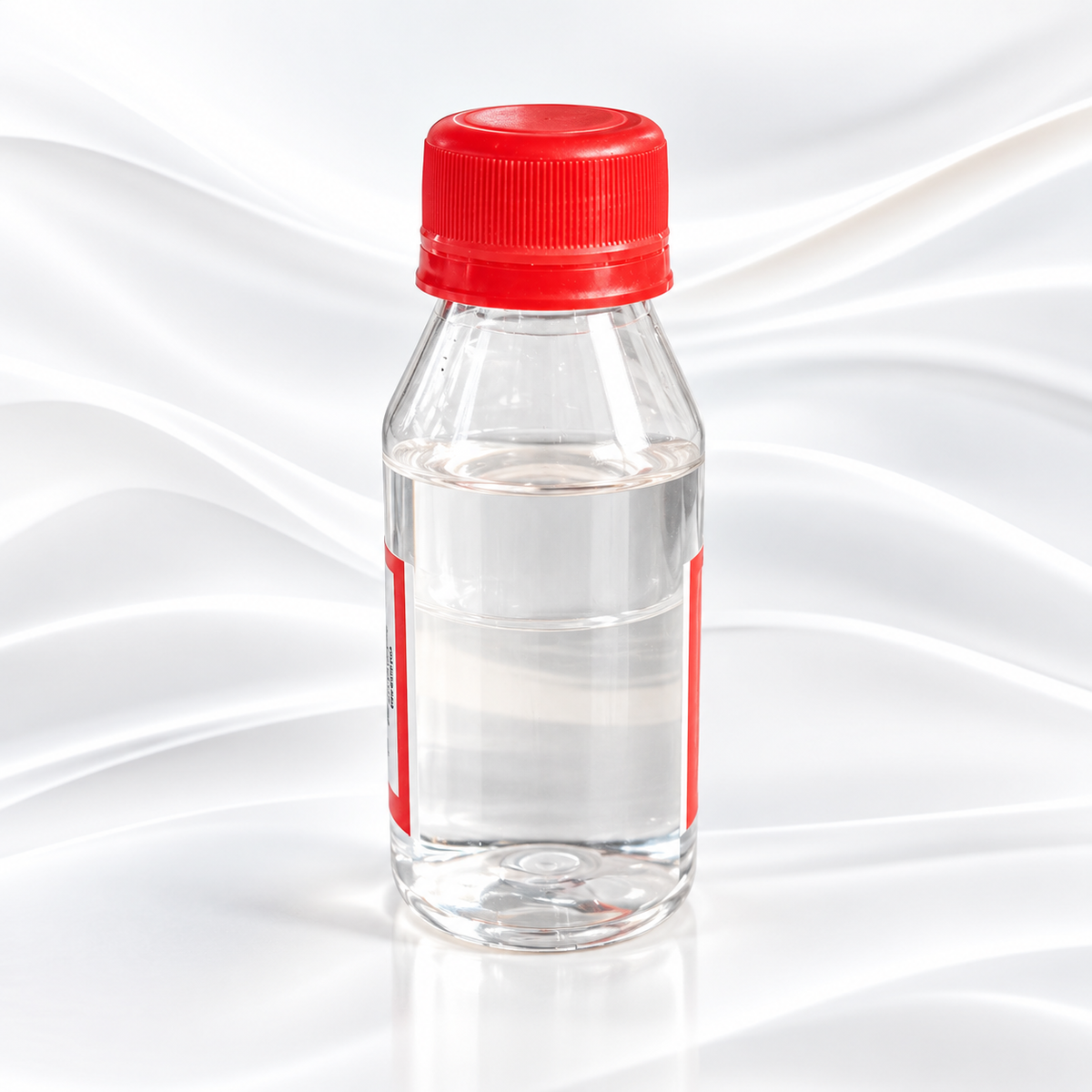 A clear plastic bottle filled with transparent liquid, featuring a bright red screw cap and a red label band, set against a white satin-like fabric background.