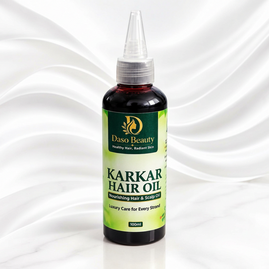 A 100ml bottle of Daso Beauty Karkar Hair Oil, featuring a dark amber glass bottle with a green and white label, a silver ribbed cap, and a clear plastic dropper tip, set against a white marble background with soft white fabric folds.