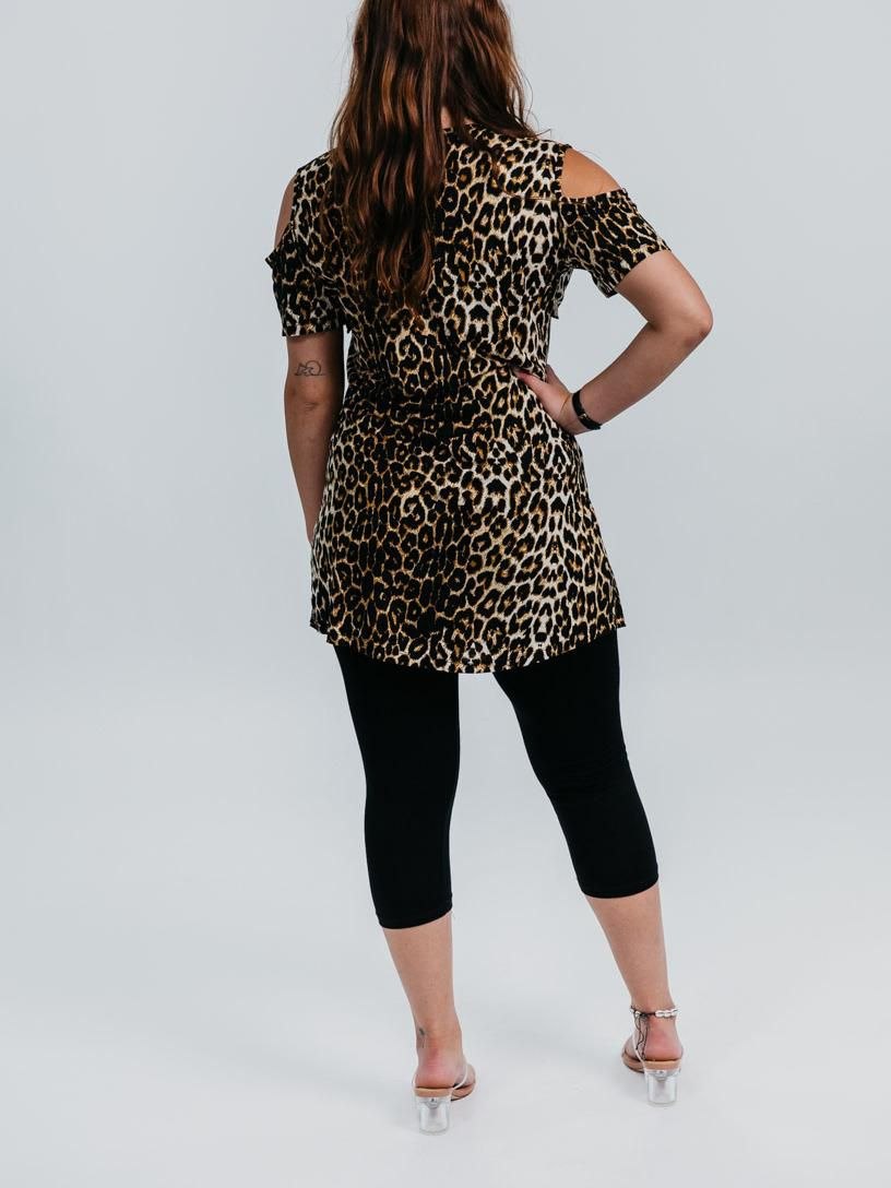 A woman shown from the back wearing a leopard print cold-shoulder tunic top with black capri leggings and clear high-heeled sandals, set against a plain light gray studio background.