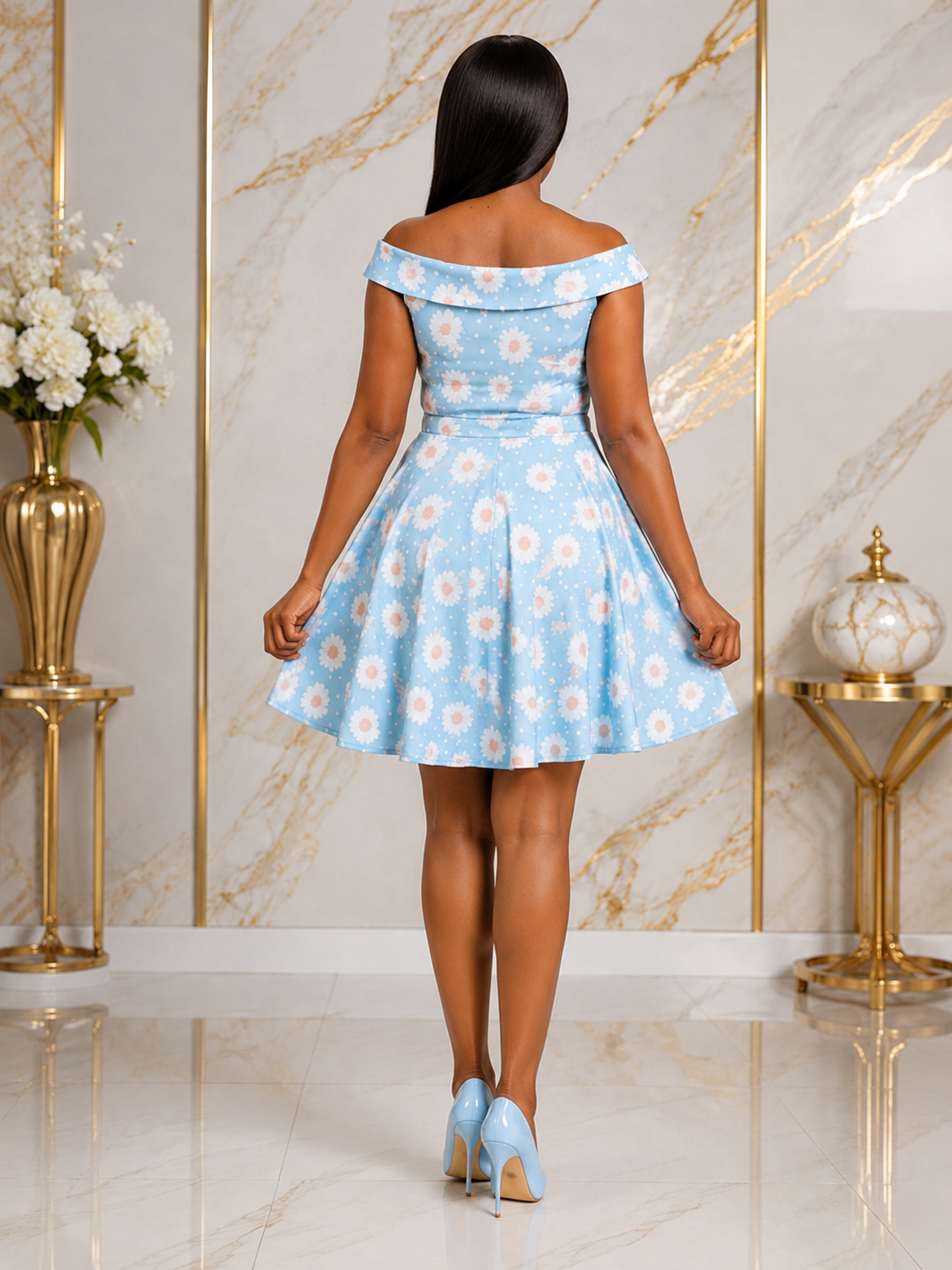 A woman stands with her back to the camera wearing a light blue off-the-shoulder fit-and-flare dress with a white floral pattern, paired with light blue high heels, in front of a marble wall with gold accents.
