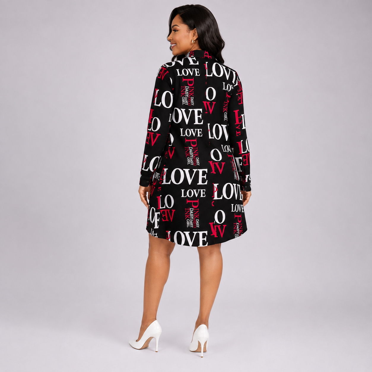 A woman modeling a black long-sleeve shirt dress with a white and red 'LOVE' text pattern, shown from a back-three-quarter angle against a light gray studio background.
