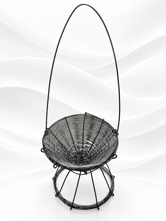 A black metal hanging basket chair with a woven seat and a tall arched handle, shown against a white wavy studio background.