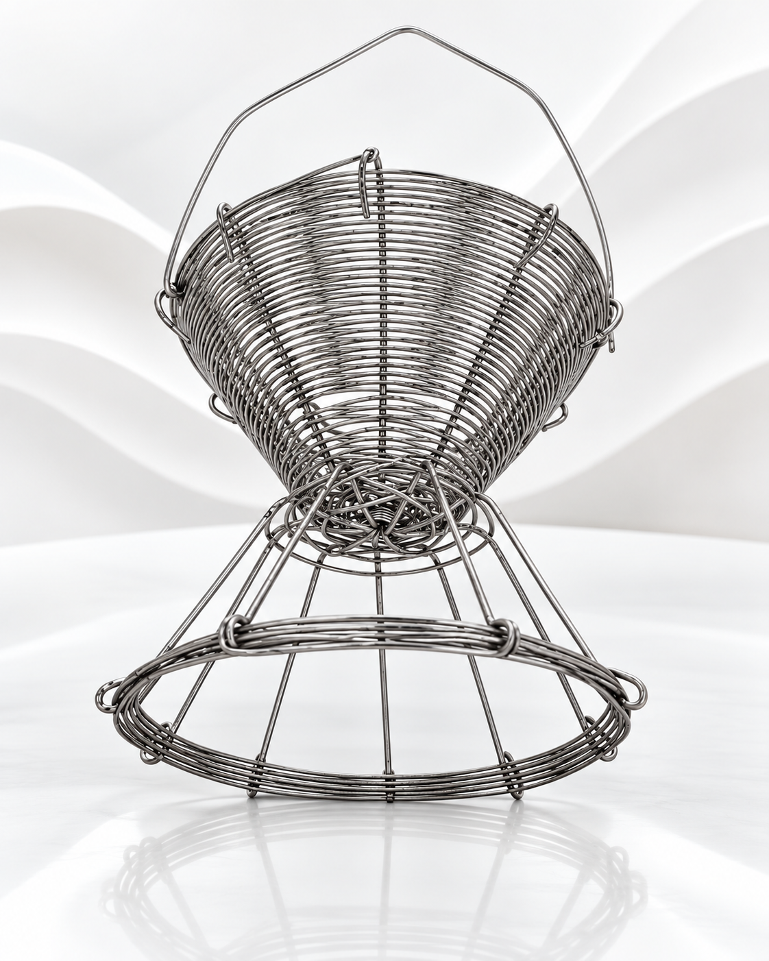 A metallic silver wire basket with a handle and a lower decorative ring, photographed on a clean white background with a soft reflection below.