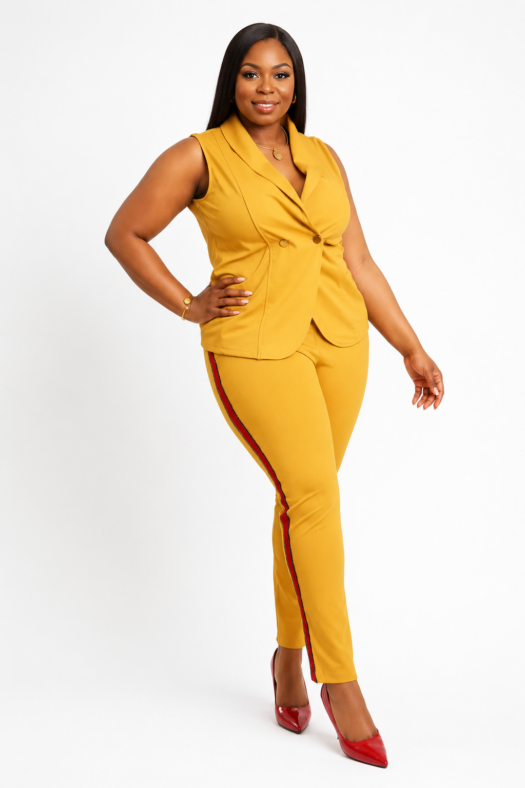 A woman modeling a mustard yellow two-piece suit consisting of a sleeveless wrap-style blazer and matching slim-fit trousers with red side stripes, paired with red pointed-toe heels, against a plain white studio background.