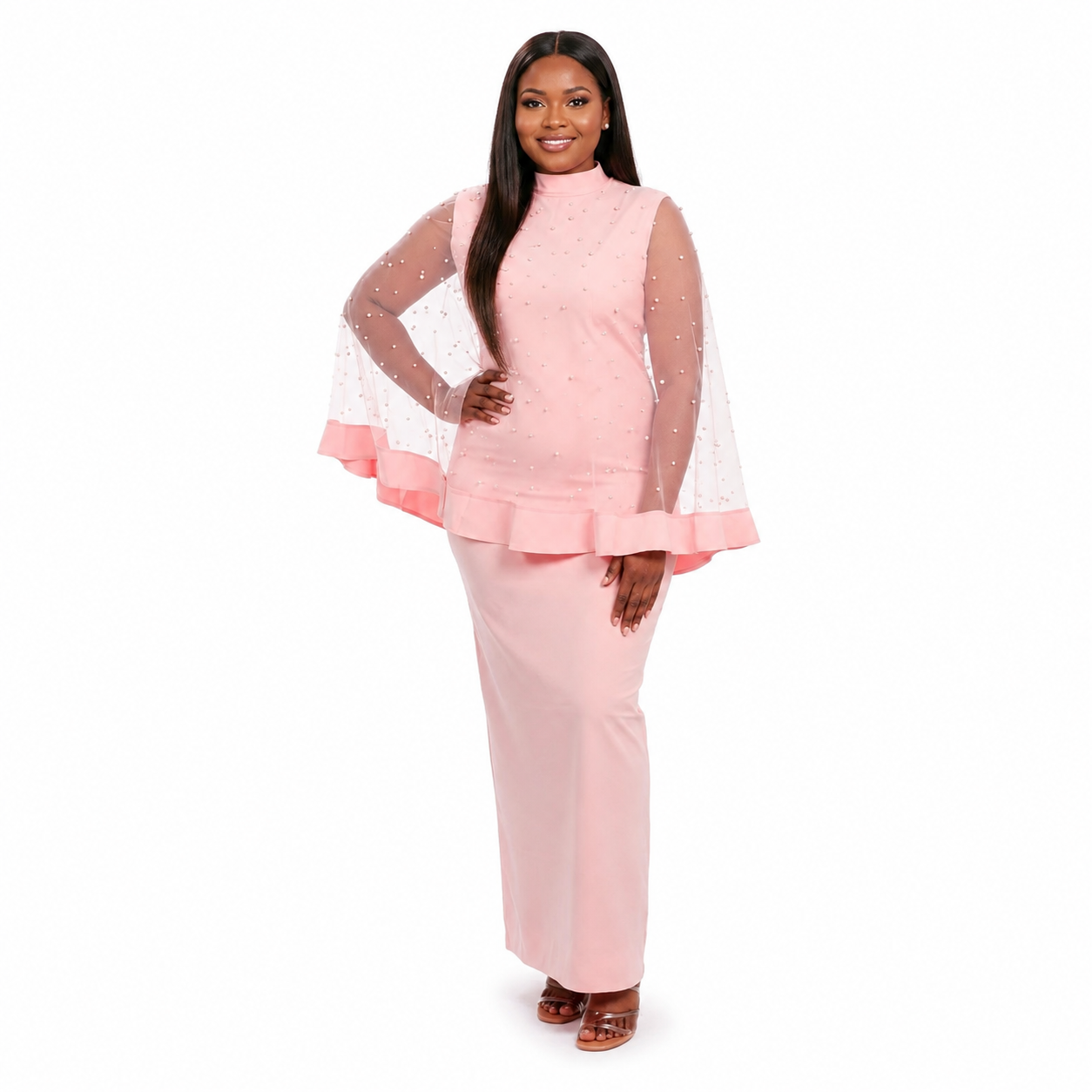 A woman modeling a light pink two-piece outfit consisting of a mock-neck long-sleeve top with sheer flutter sleeves and a matching high-waisted maxi skirt, set against a plain white background.