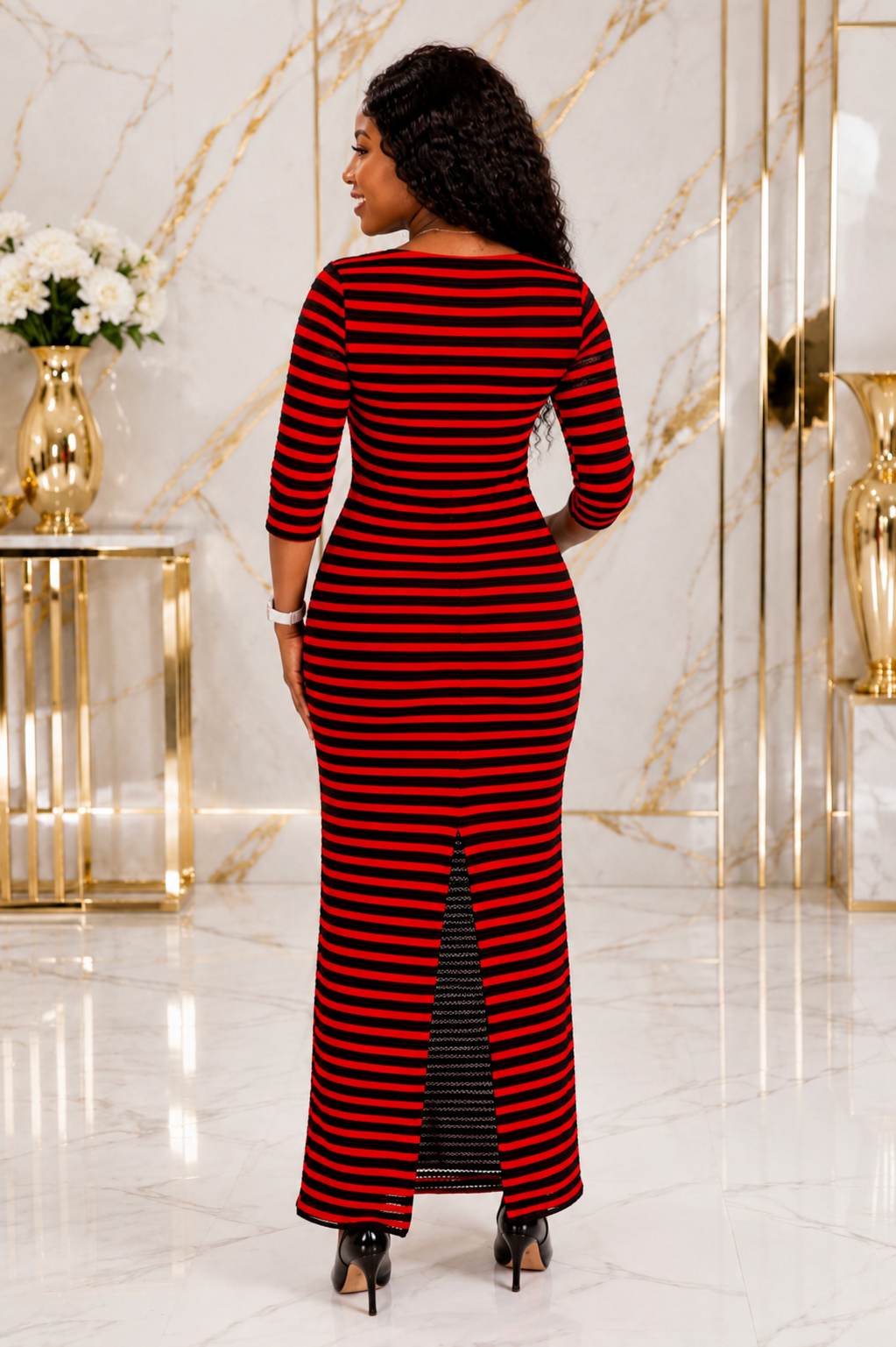 A woman wearing a red and black horizontally striped maxi dress, shown from the back in a luxurious interior with gold accents and marble walls.