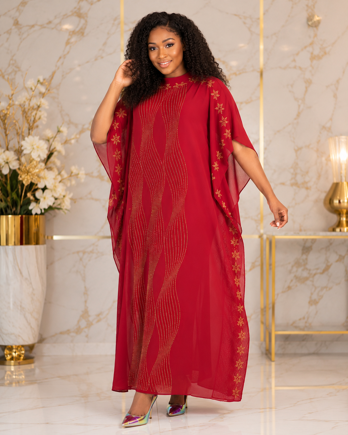 A woman modeling a long red caftan dress with gold embroidered star patterns and wavy gold line details, set against a marble and gold interior background.