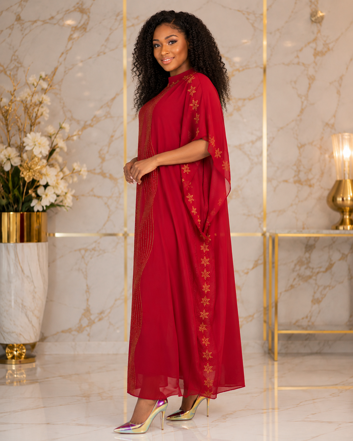 A woman modeling a long red caftan dress with gold floral embroidery down the side, standing in a luxurious room with marble walls and gold accents.