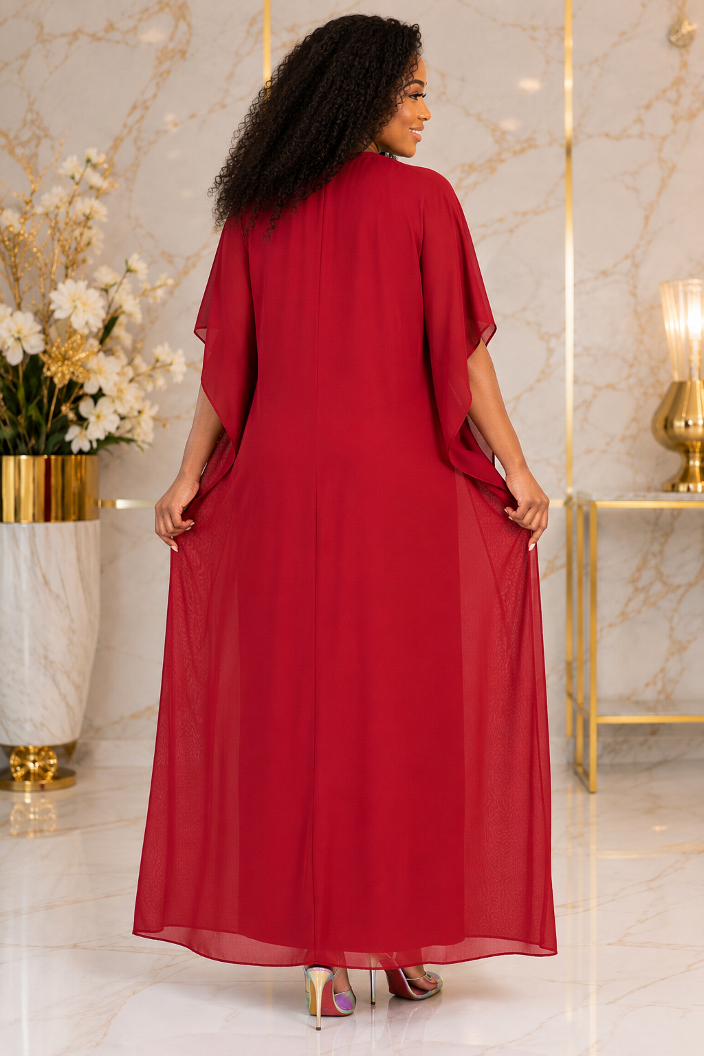 A woman viewed from behind wearing a flowing red maxi dress with draped short sleeves, standing in a luxurious interior with marble walls and gold accents.
