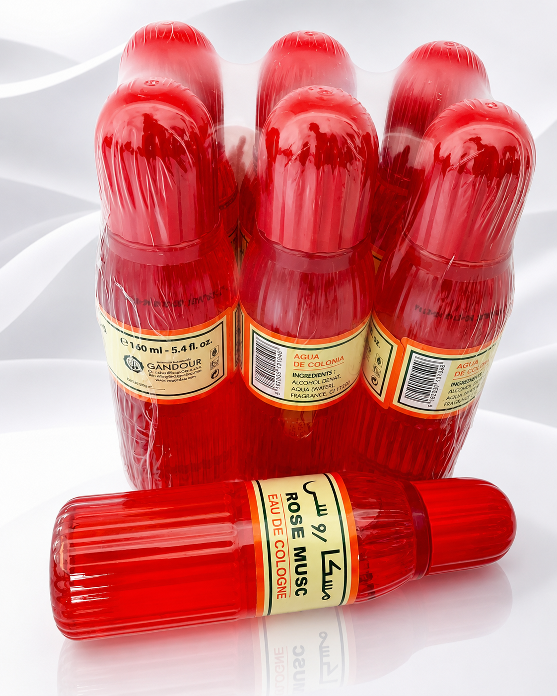 Six red perfume bottles wrapped in clear plastic, with one bottle lying in front and five standing behind it on a white reflective surface.