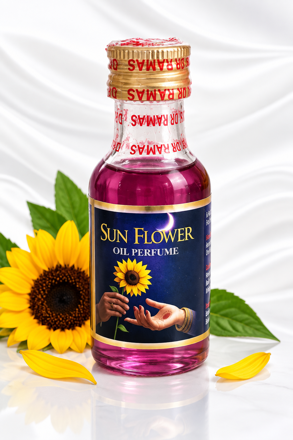 A bottle of Ramas Sun Flower Oil Perfume with a dark blue label and gold accents, filled with pink liquid. The bottle is styled with a yellow sunflower, green leaves, and yellow petals on a white draped satin background.