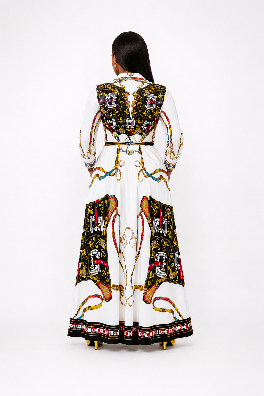 A model viewed from the back wearing a long white coat with elaborate black, gold, red, and blue baroque-style ornamental patterns and a decorative border, set against a plain white studio background.