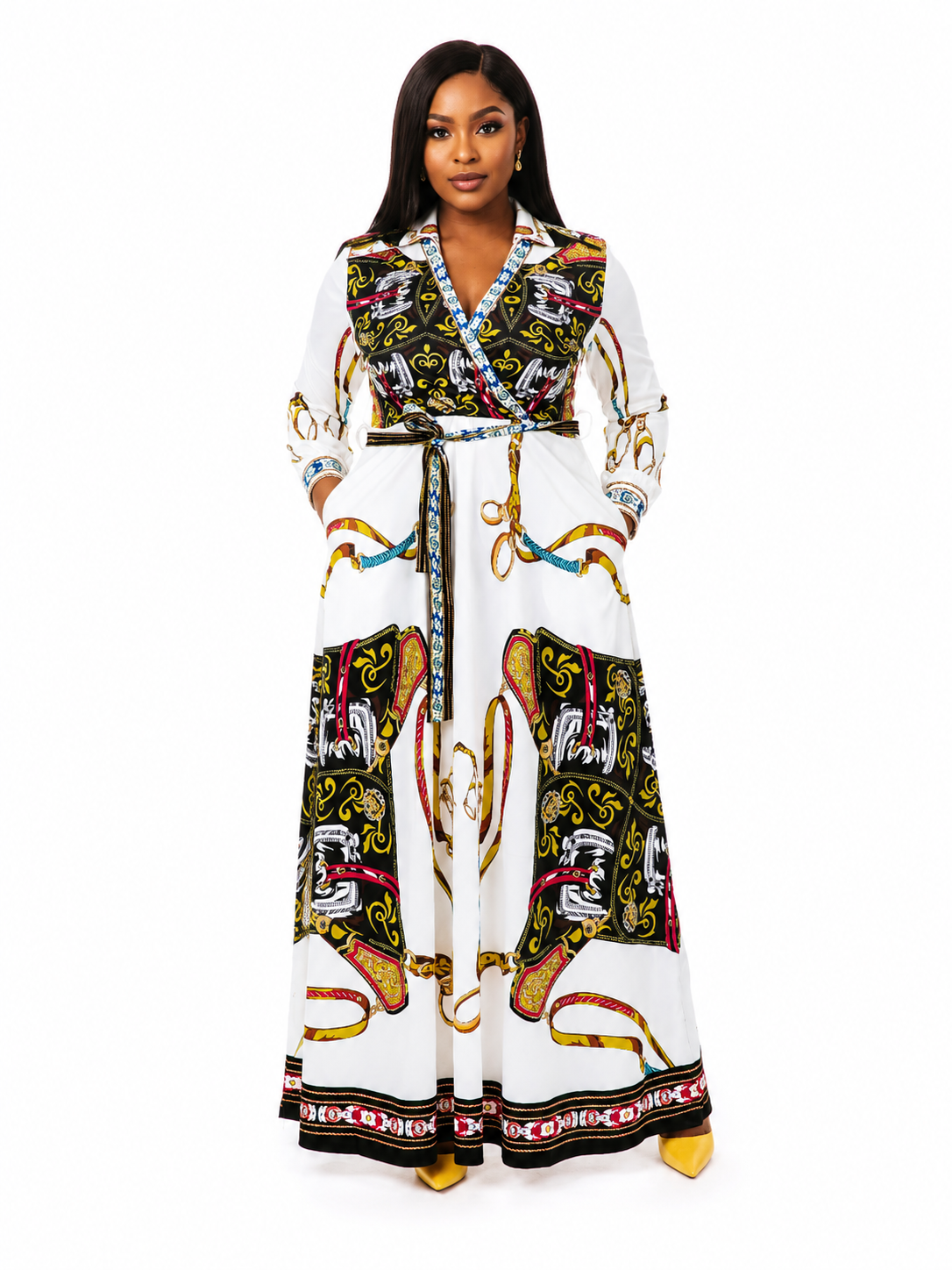 A woman modeling a long white maxi dress with a bold black, gold, and red graphic print, featuring a V-neck, waist tie, and three-quarter sleeves, set against a plain white background.