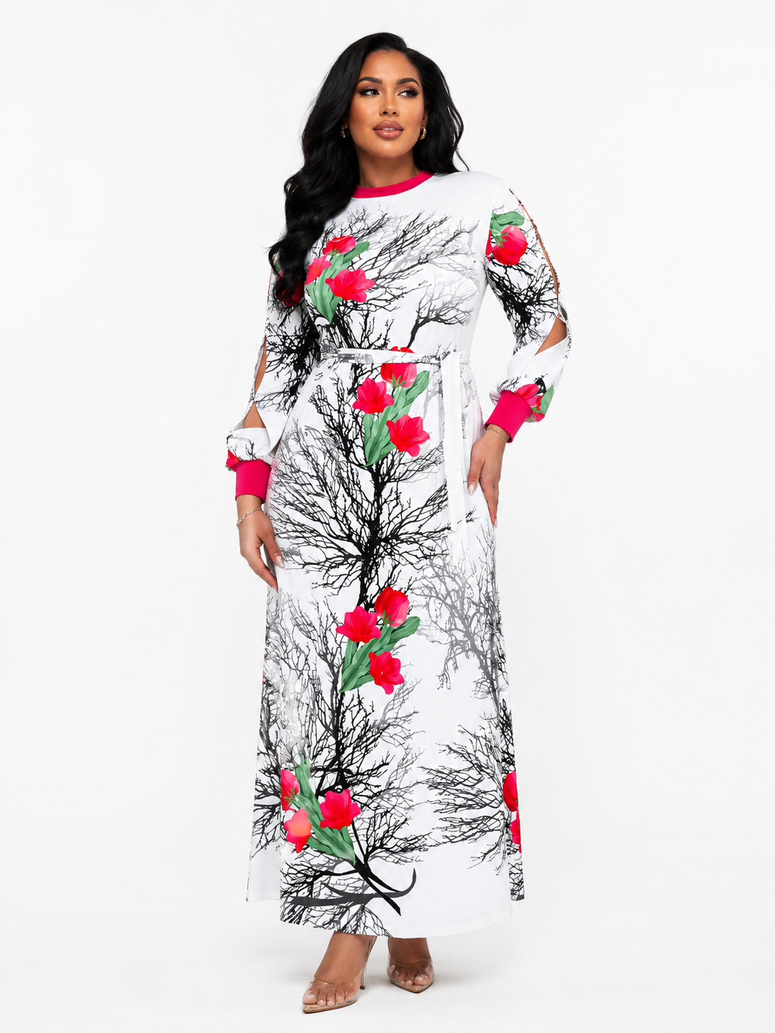 A woman modeling a long white maxi dress with a black branch pattern and bright red rose prints, featuring cutout sleeves and a matching belt, set against a plain white studio background.