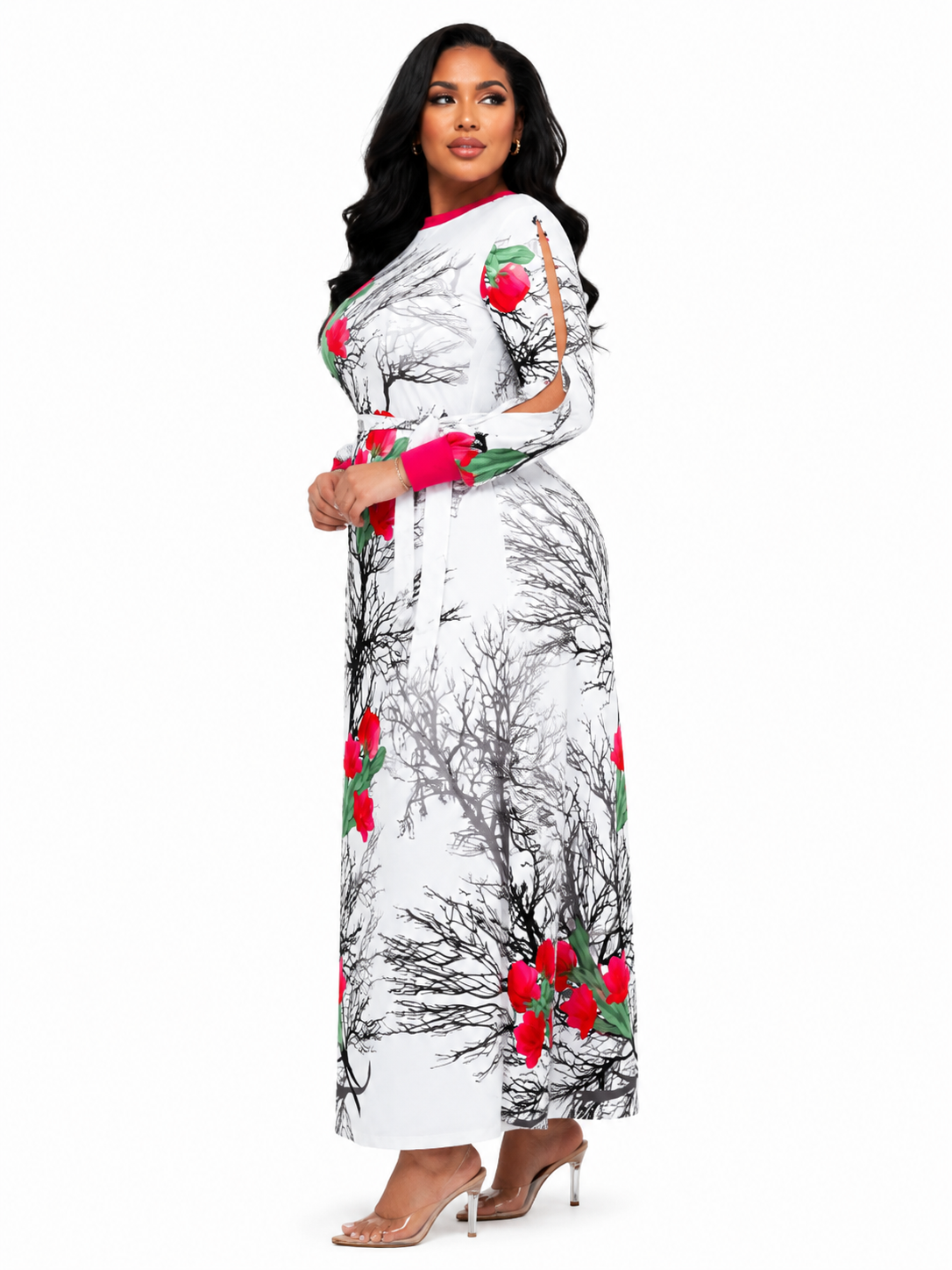A woman modeling a long white dress with a black tree branch print and red floral accents, paired with clear high-heeled sandals, against a plain white background.