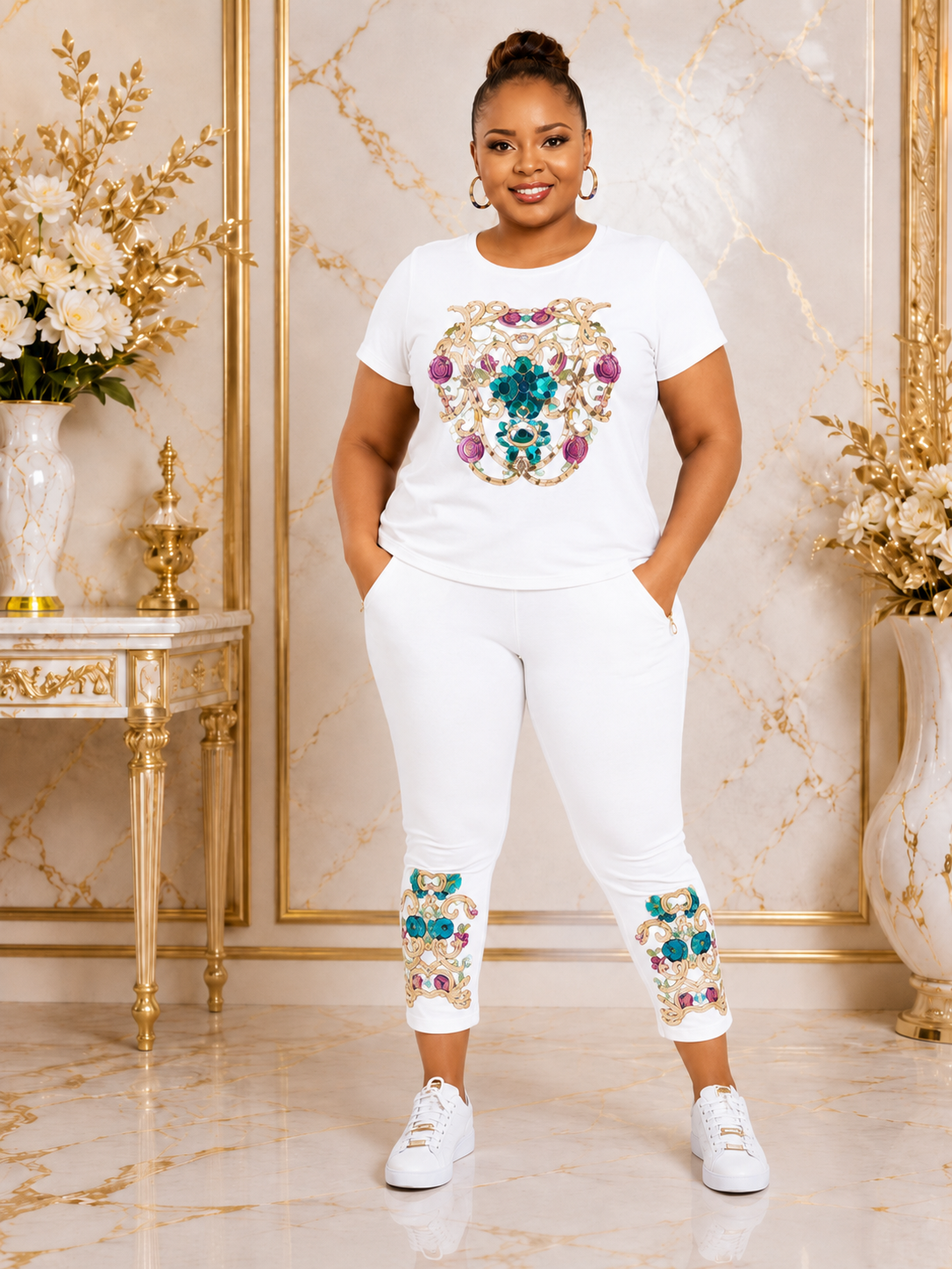 A woman modeling a white two-piece loungewear set featuring a large embroidered crest on the t-shirt and matching embroidered cuffs on the pants, set against a luxurious gold and beige marble background.