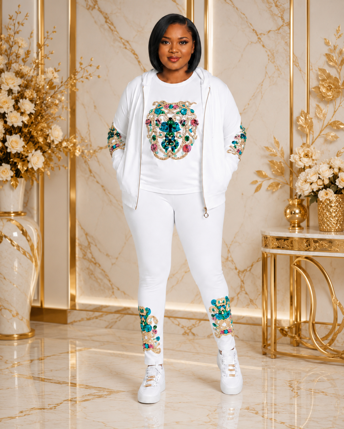 A woman modeling a white three-piece tracksuit with colorful floral embroidery, standing in a luxurious room with gold accents and marble floors.