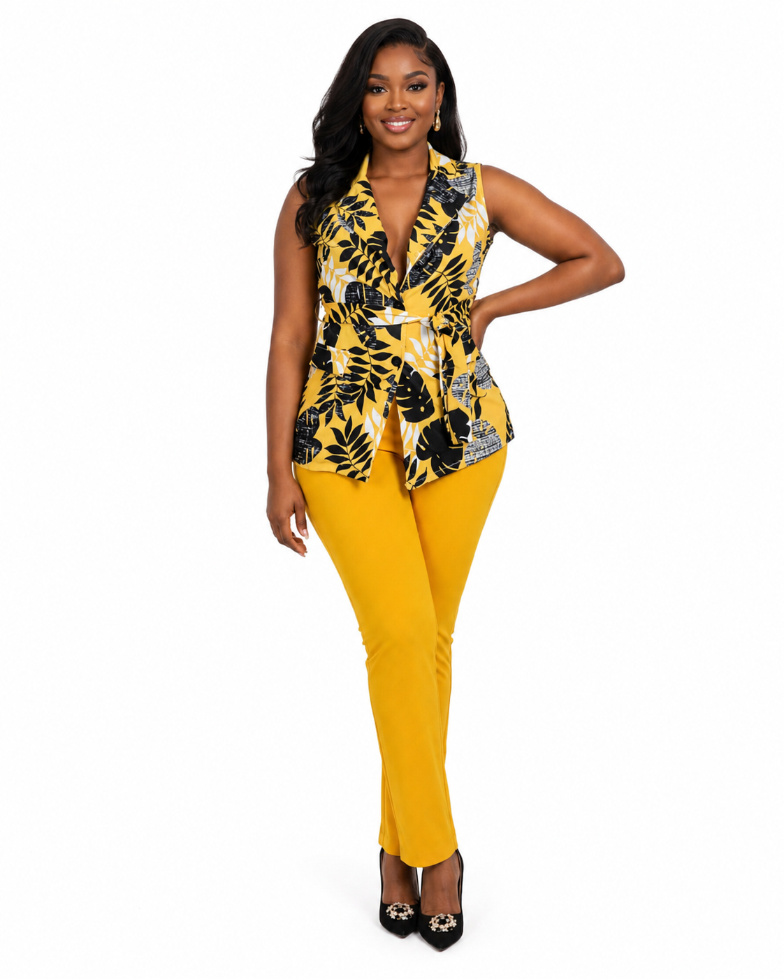 A woman modeling a sleeveless wrap-style top with a yellow, black, and white tropical leaf print, paired with bright yellow pants and black heels, against a plain white background.